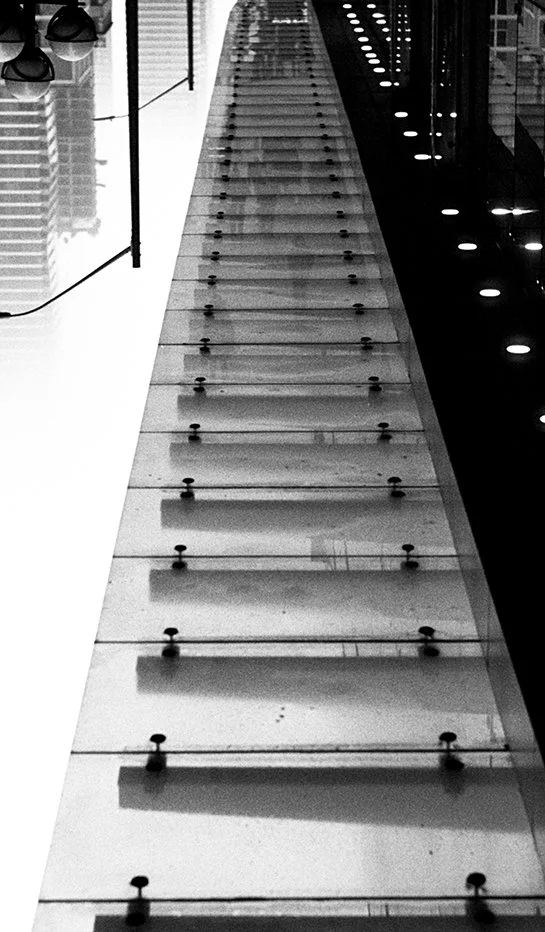 A close-up view of a glass staircase with metal supports in a modern building, viewed from above.