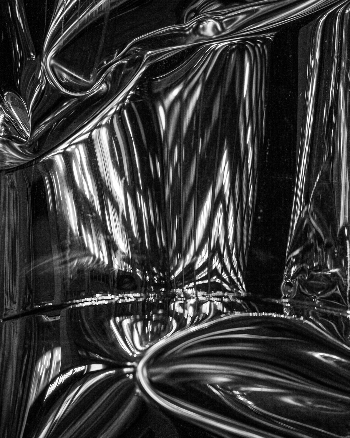 Close-up of a crumpled, shiny metallic, reflective surface, possibly foil or metallic fabric, with intricate folds and reflections.