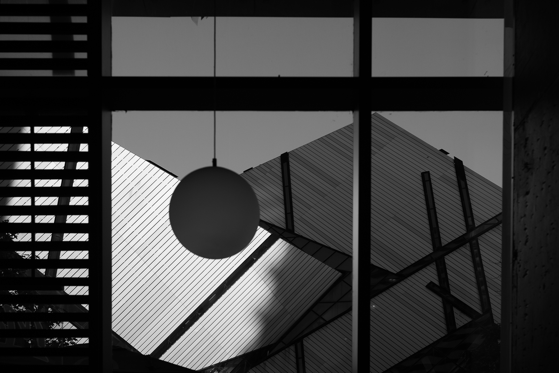 Black and white photo of modern building architecture with slanted roofs, a circular hanging lamp, and window pane frames.