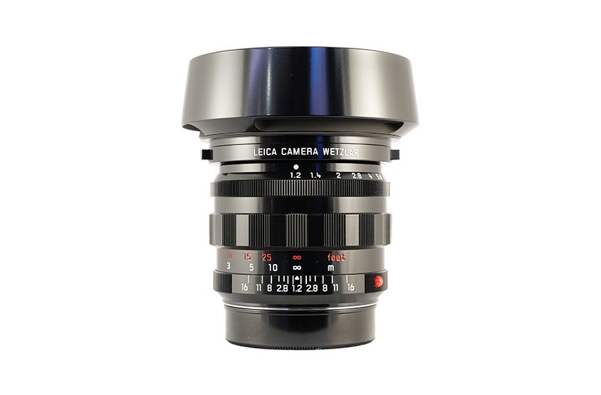 A Leica camera lens with various focus and aperture markings, placed under a metallic shade.