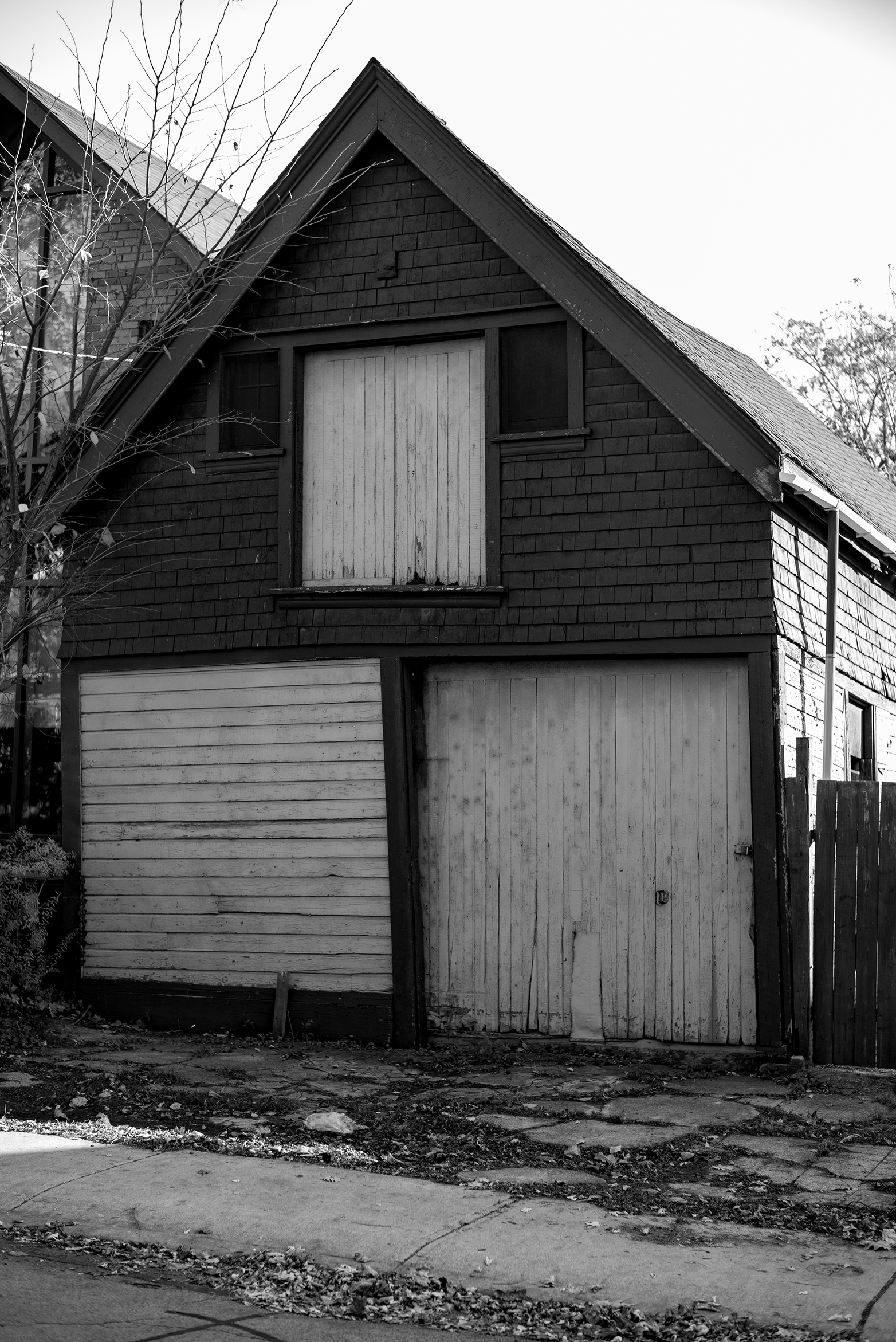A black and white photo of an old, abandoned garage with a weathered wooden door and boarded-up upstairs windows.