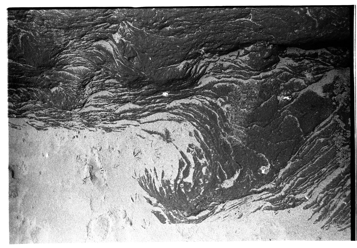 Close-up of layered, textured rock formation and footprints in the sand.