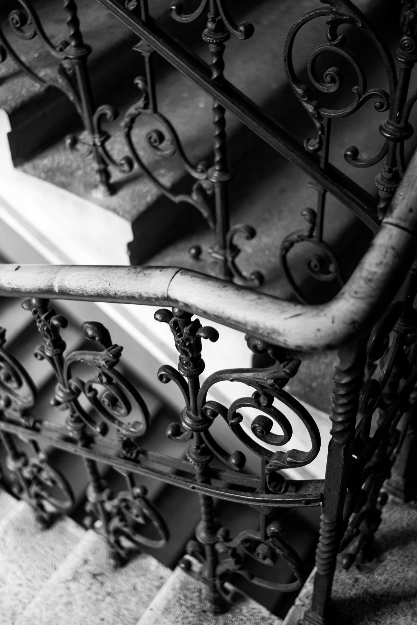 Black and white photo of an ornate, vintage staircase with intricate wrought iron railings and a stone handrail.