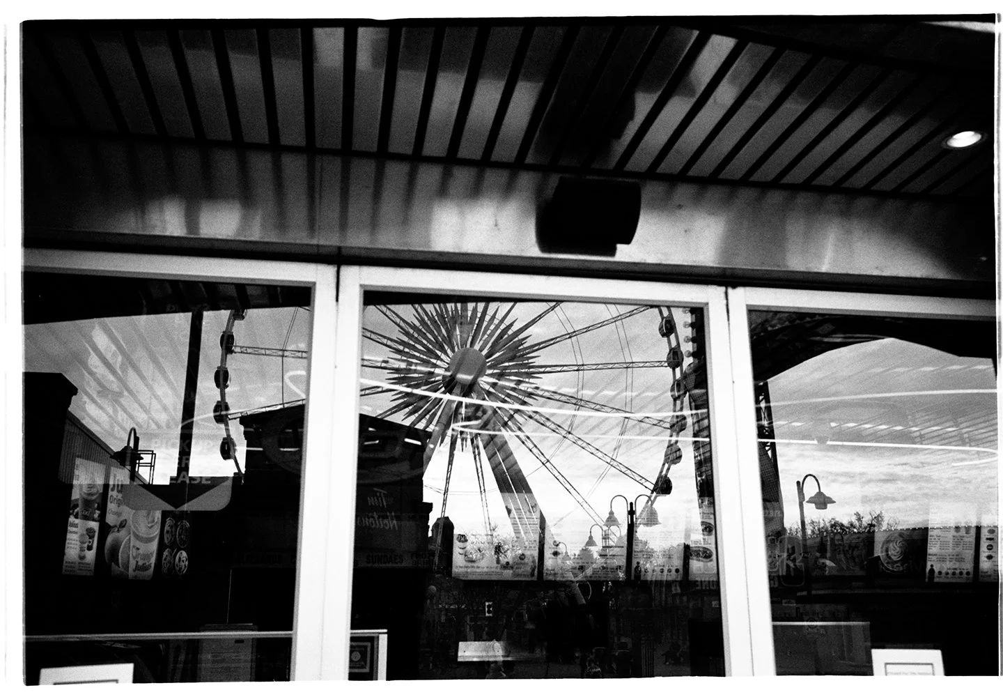 Reflection of a large Ferris wheel seen through the window of a building with a wooden ceiling.
