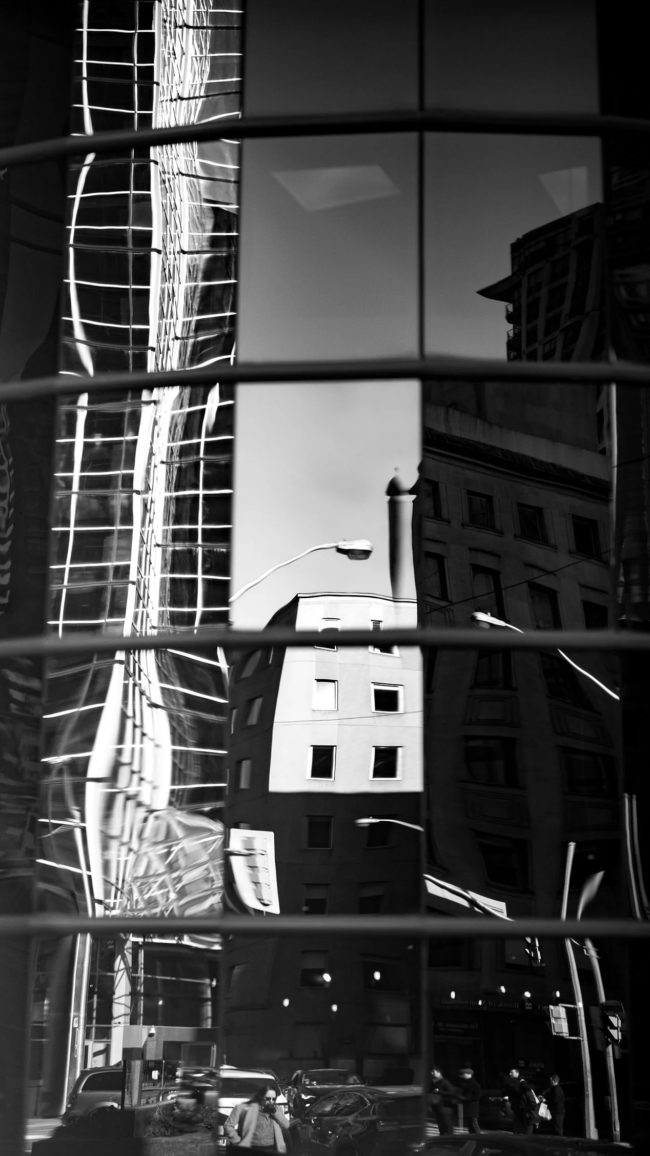 Reflection of city buildings, streetlights, and pedestrians in a glass window with horizontal bars in black and white