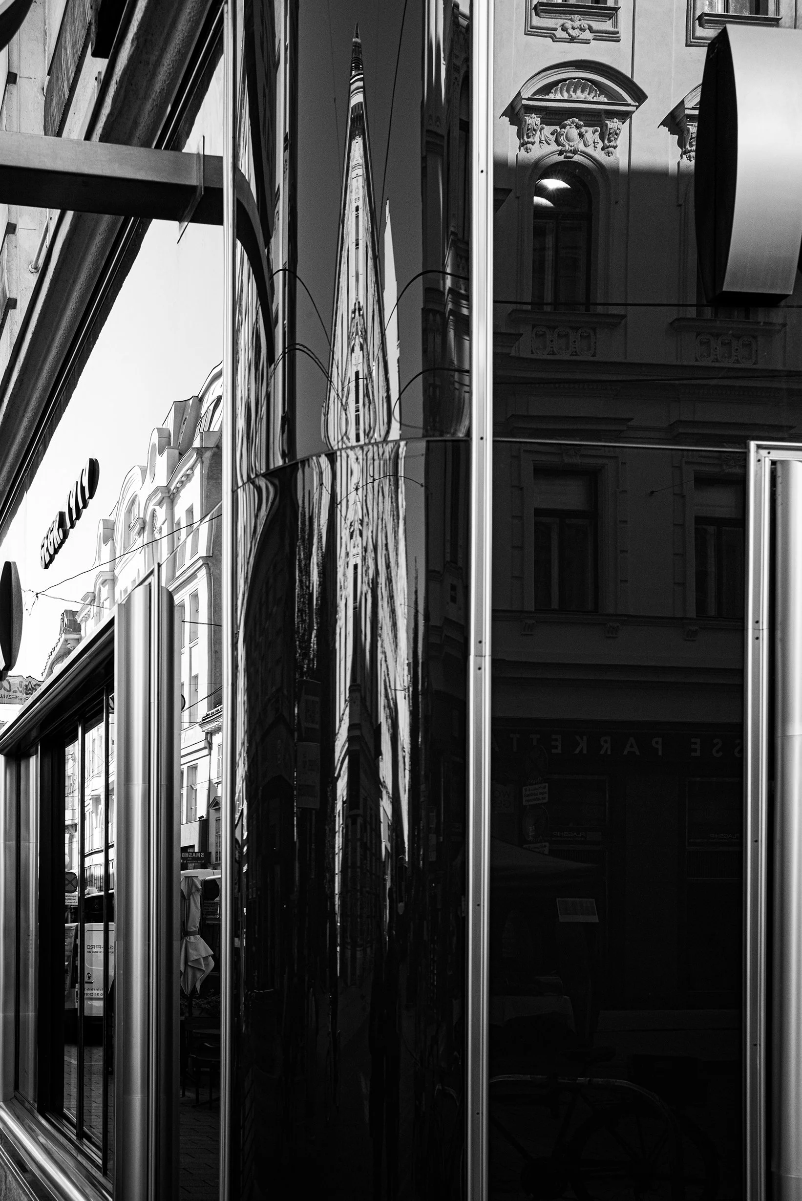 Reflection of a church steeple and surrounding buildings on the black glossy surface of a modern building with large glass windows.