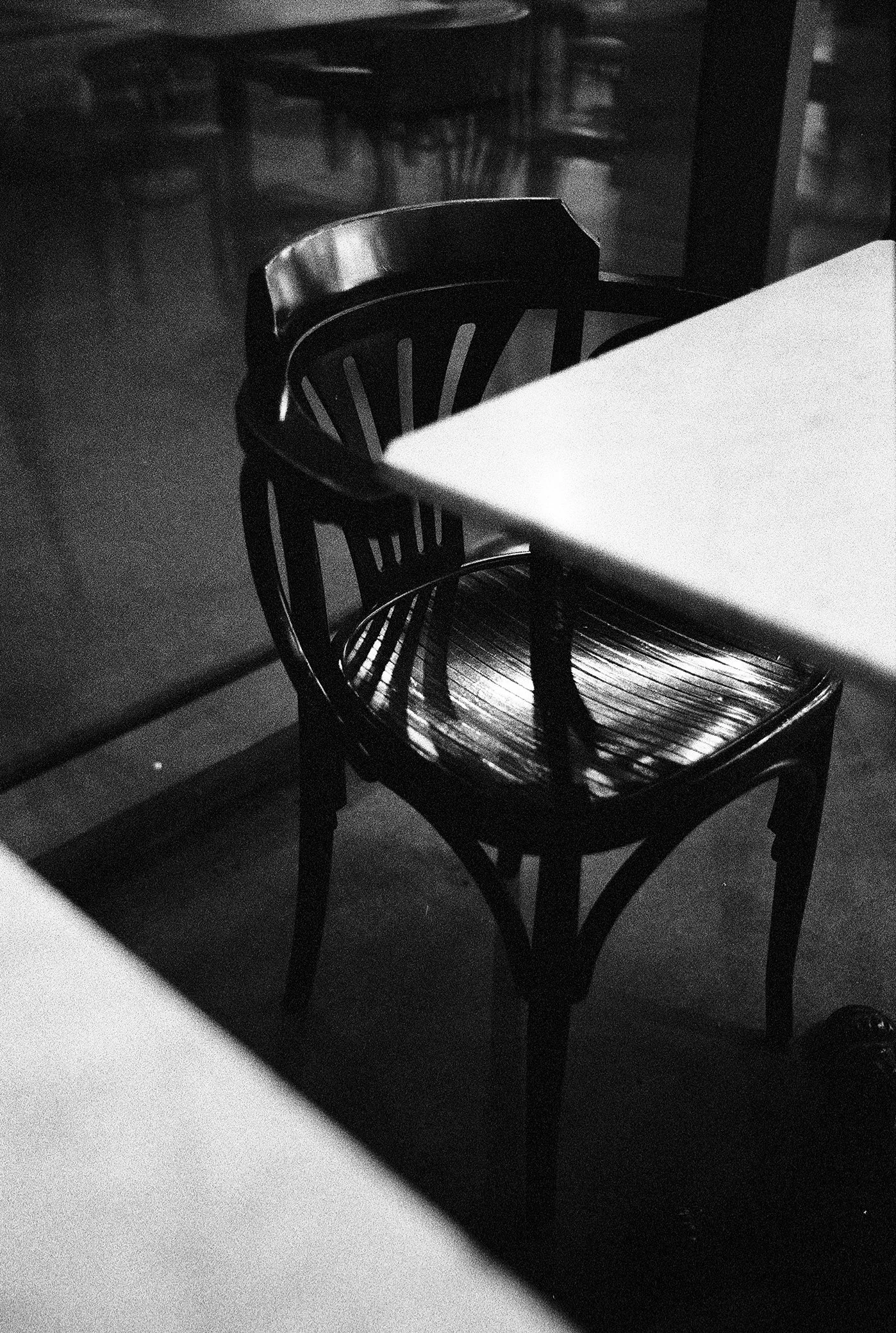 Black wooden chair at a table in a dimly lit environment with reflections on the floor.