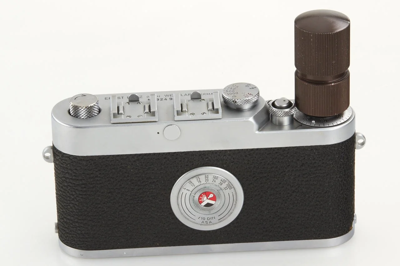 A vintage black and silver camera with a brown lens and various dials and buttons on the top.