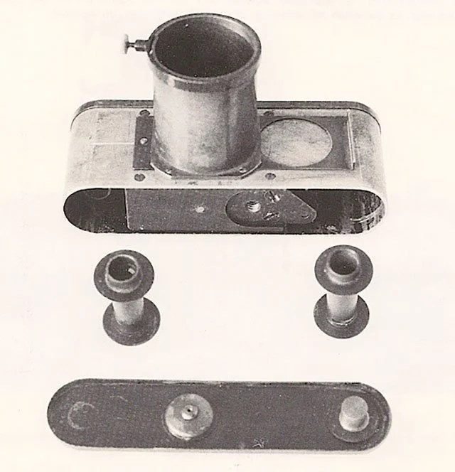 Disassembled vintage camera parts, including a lens, body, and lens caps, laid out on a plain background.