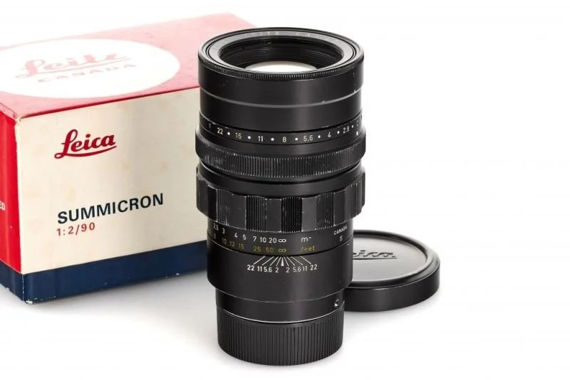 Leica Summicron camera lens with mount cap in front of its red and white box.