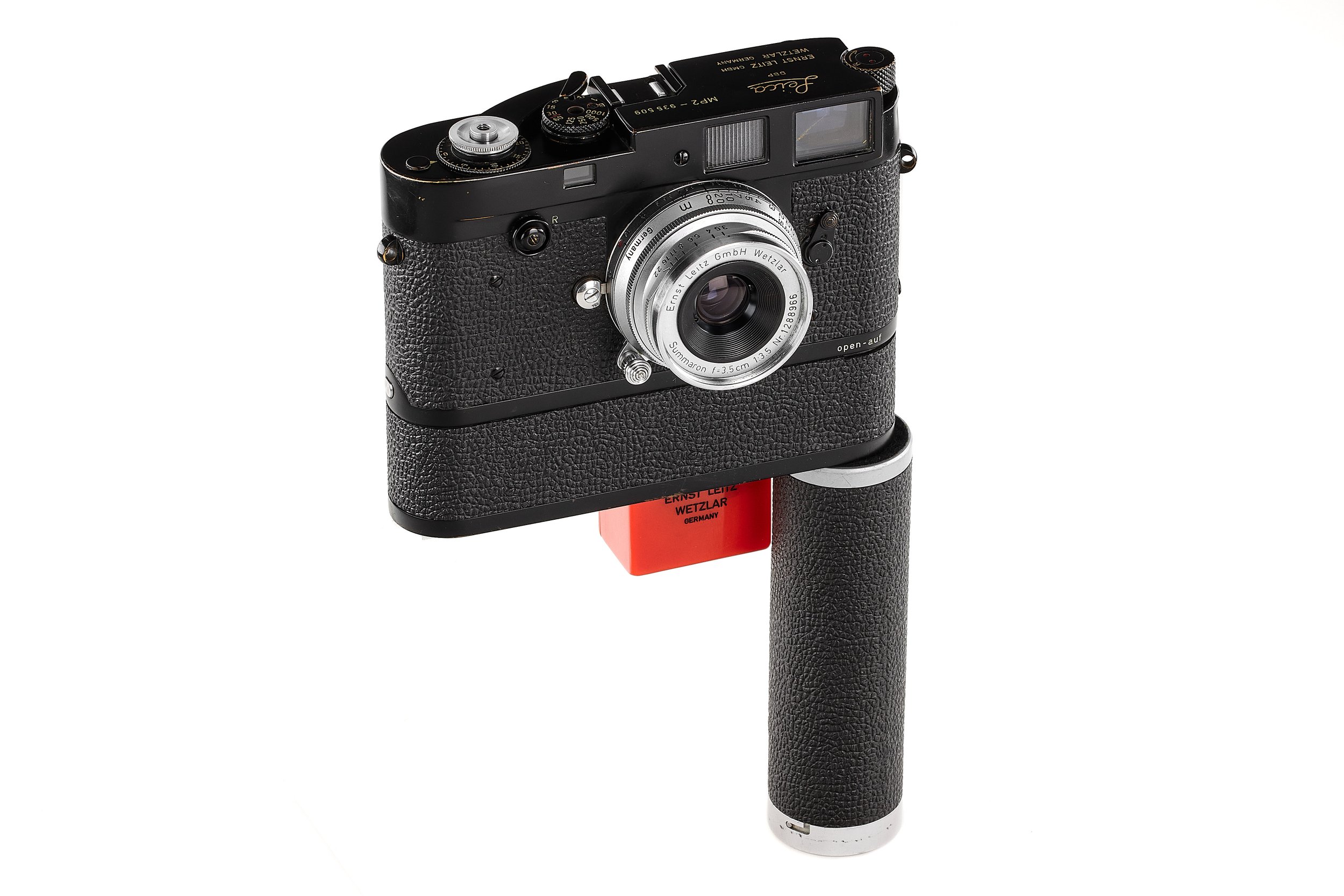 A vintage Leica camera mounted on a red tripod handle against a white background.