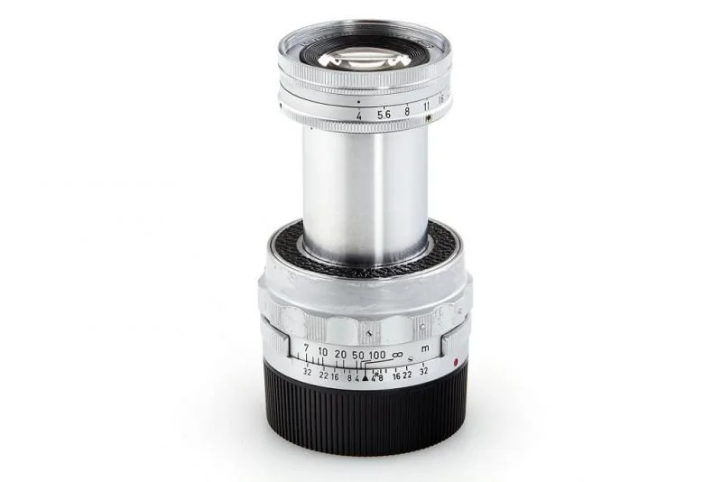A vintage camera lens with silver and black metallic parts and focus and aperture rings.