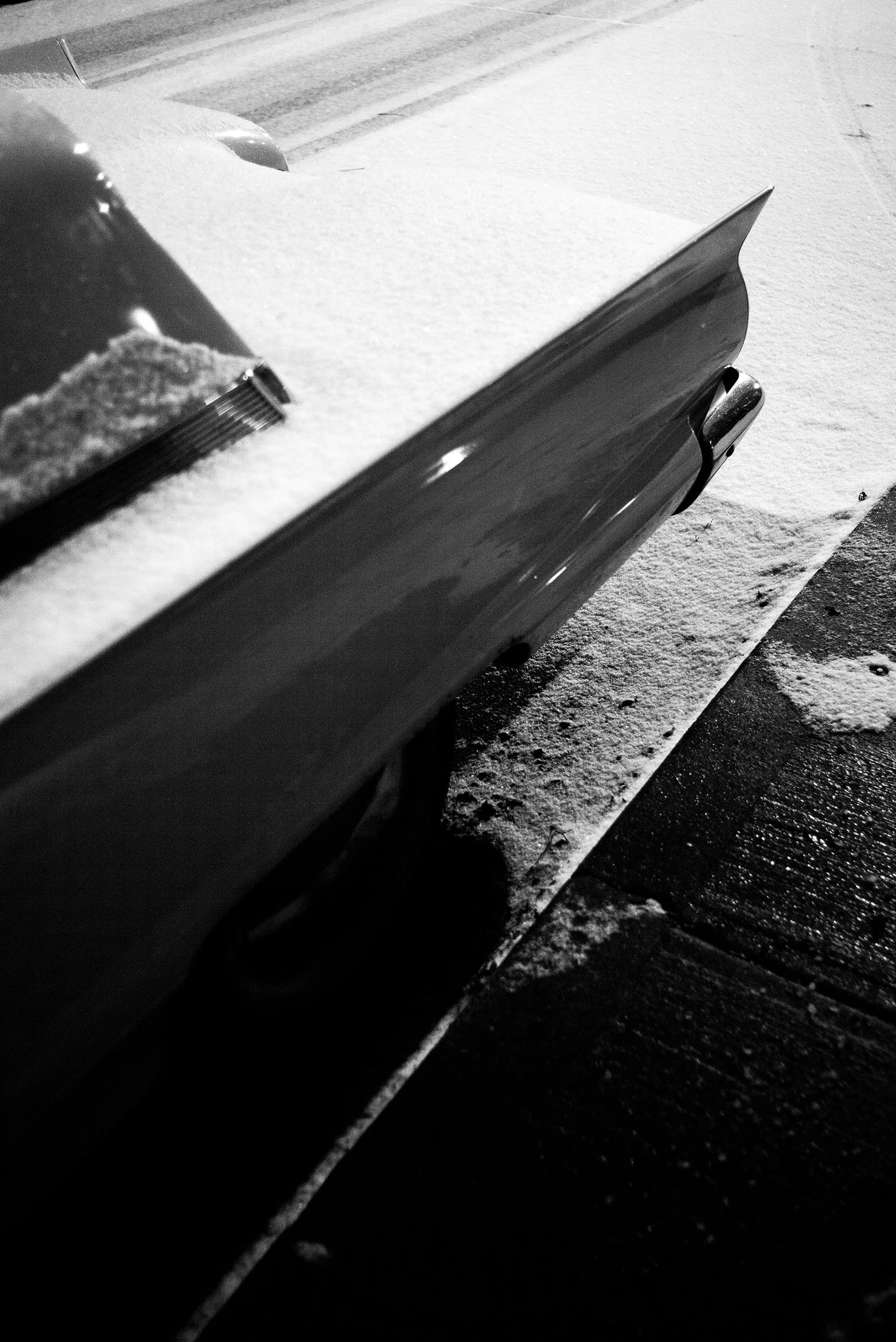 Close-up of the side of a car covered in snow, parked on a snow-covered driveway at night.