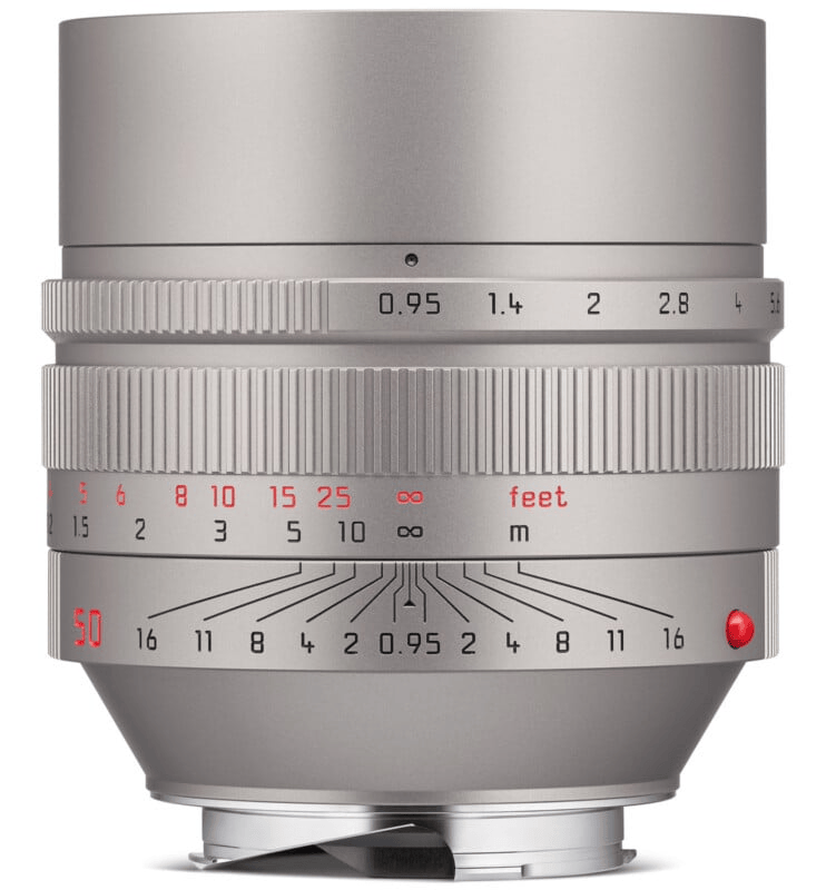 Silver camera lens with multiple focus and distance markings, including measurements in feet and meters, along with aperture scale.