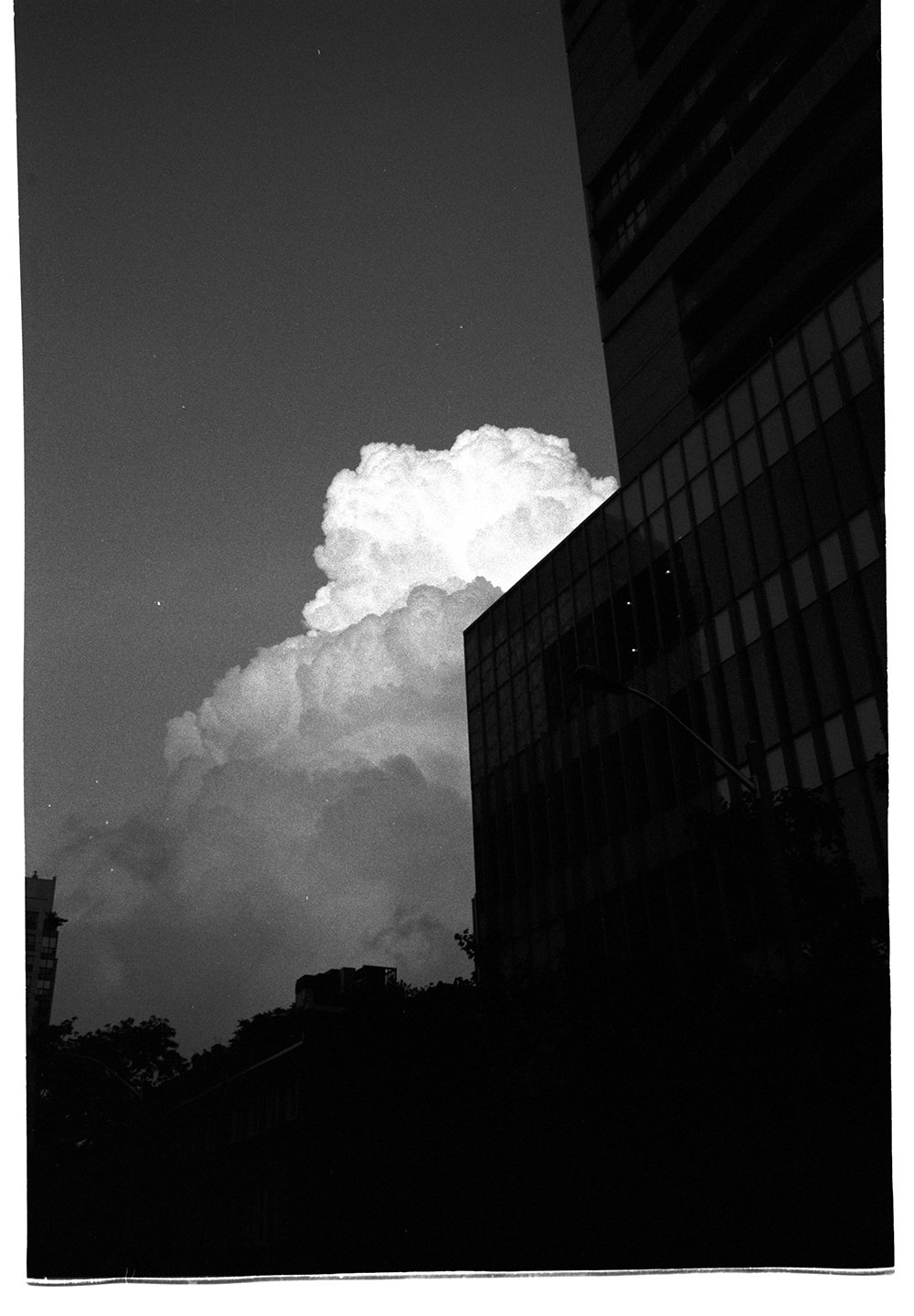 Nighttime cityscape with a partially illuminated cloud over a dark building with glass windows.