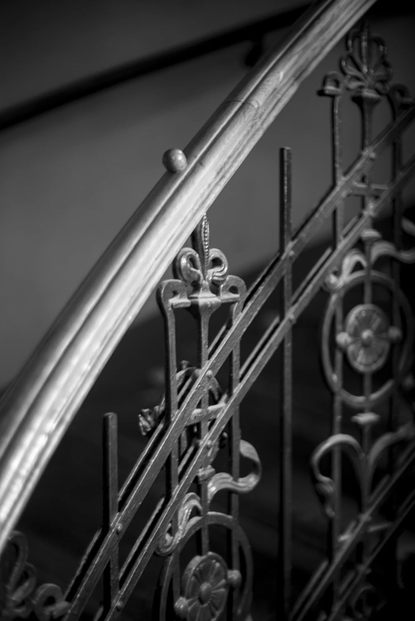 Black and white close-up of an ornate iron staircase railing with decorative floral motifs.