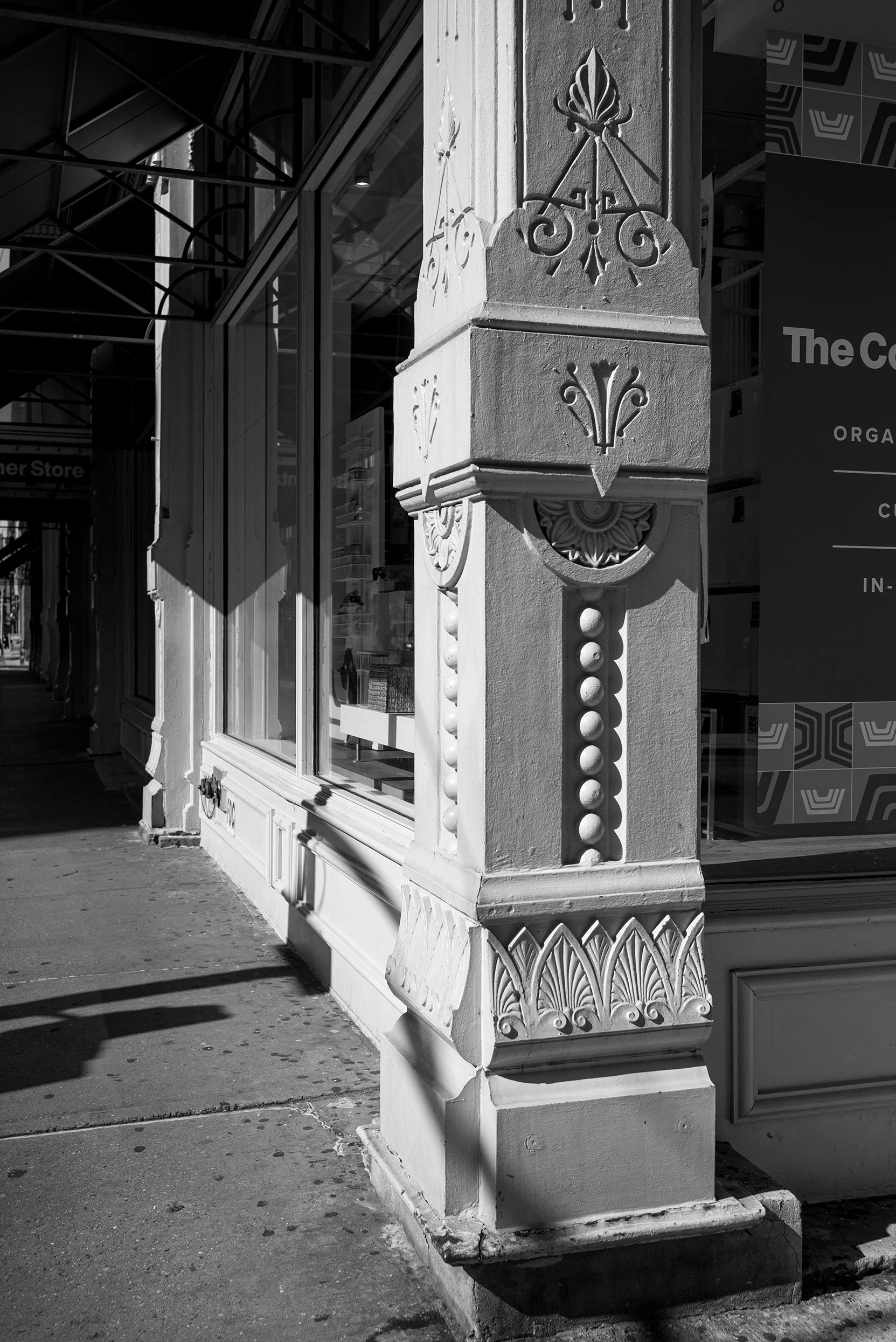 Black and white photo of ornate architectural detail on a building corner, with decorative moldings, a carved floral motif, and a window.