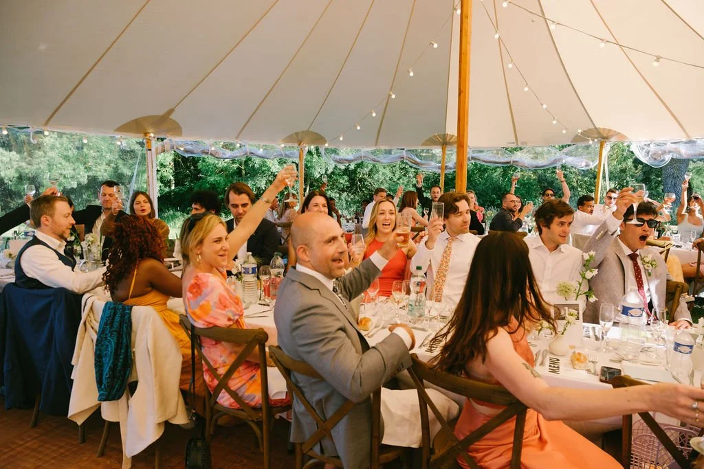 Guests at a Loustalviel wedding reception raising glasses in toast under a large tent with string lights, enjoying a celebration outdoors.