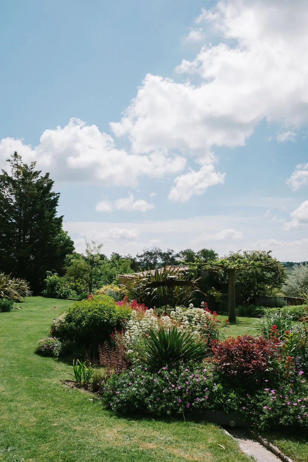 Le Domaine de Loustalviel's lush garden with blooming flowers, green grass, and trees.