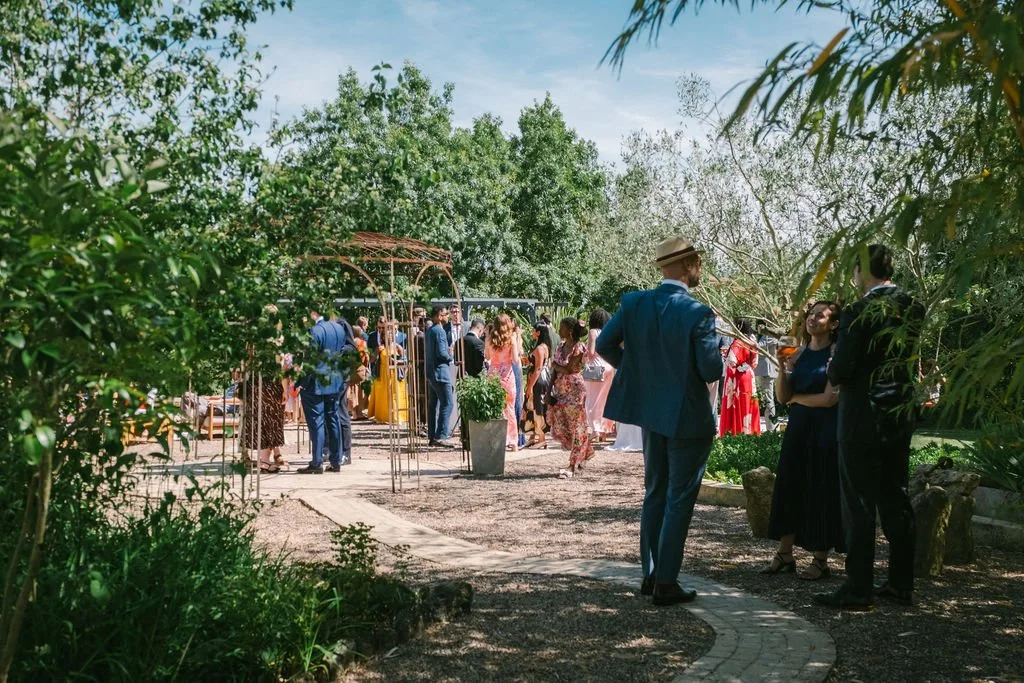 People gathered outdoors at a wedding at Le Domaine de Loustalviel, socialising and standing on a pathway with lush greenery.