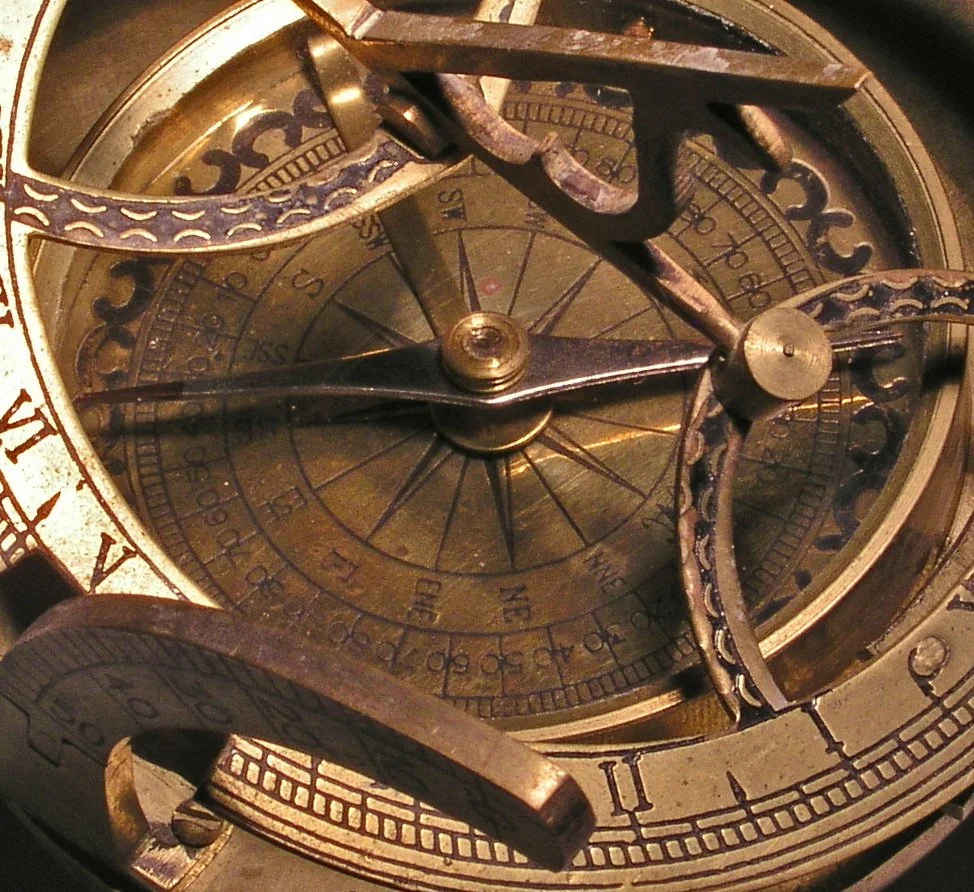 Close-up of vintage brass and steel mechanical instrument, possibly a clock or navigational device, with intricate gears, dials, and engraved markings.
