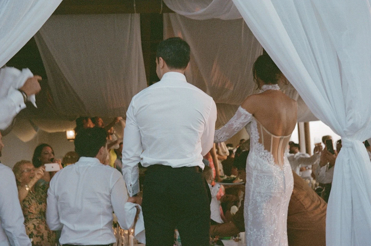 Bride and groom entering wedding reception with guests taking photos.