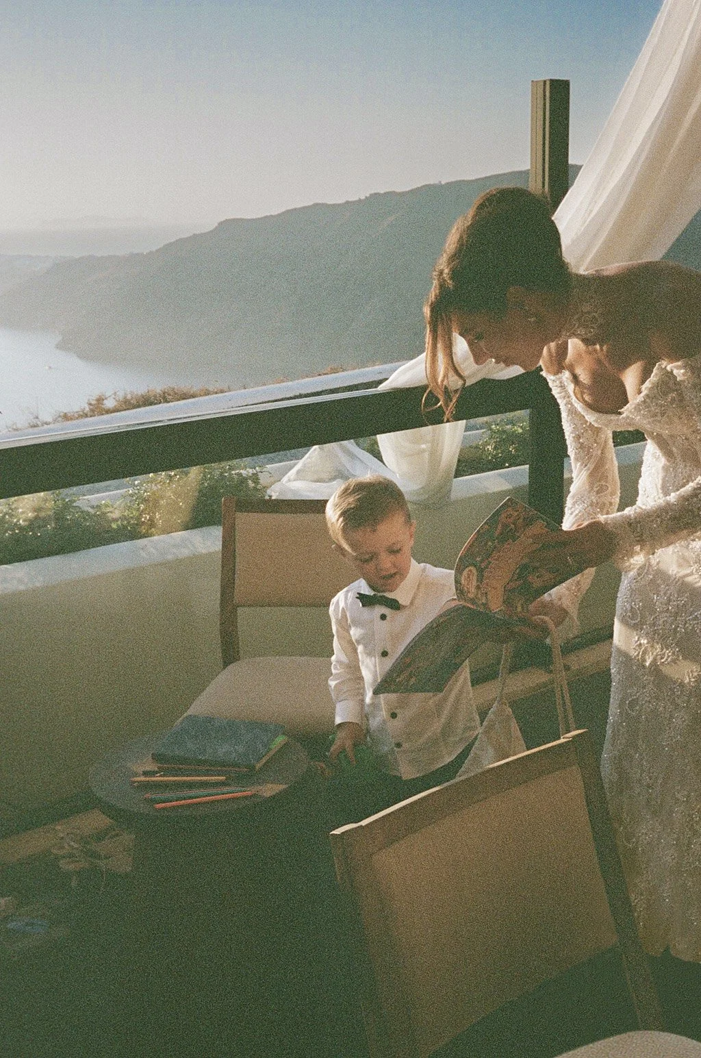 Bride in Berta Bride lace dress with her son at an outdoor setting in Santorini with an ocean view