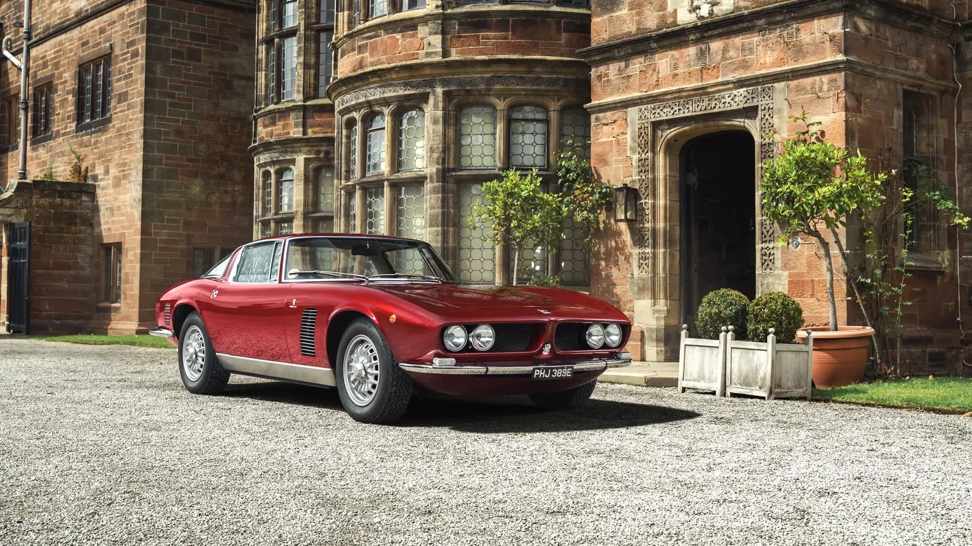 Red vintage Ferrari sports car parked outside a historic stone building with ornate windows and potted plants.