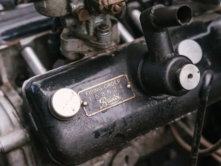 Close-up of a vintage aircraft control panel with a black metal badge labeled "Firing Order 1536244" and the brand name "Ristol," surrounded by various mechanical parts and controls.