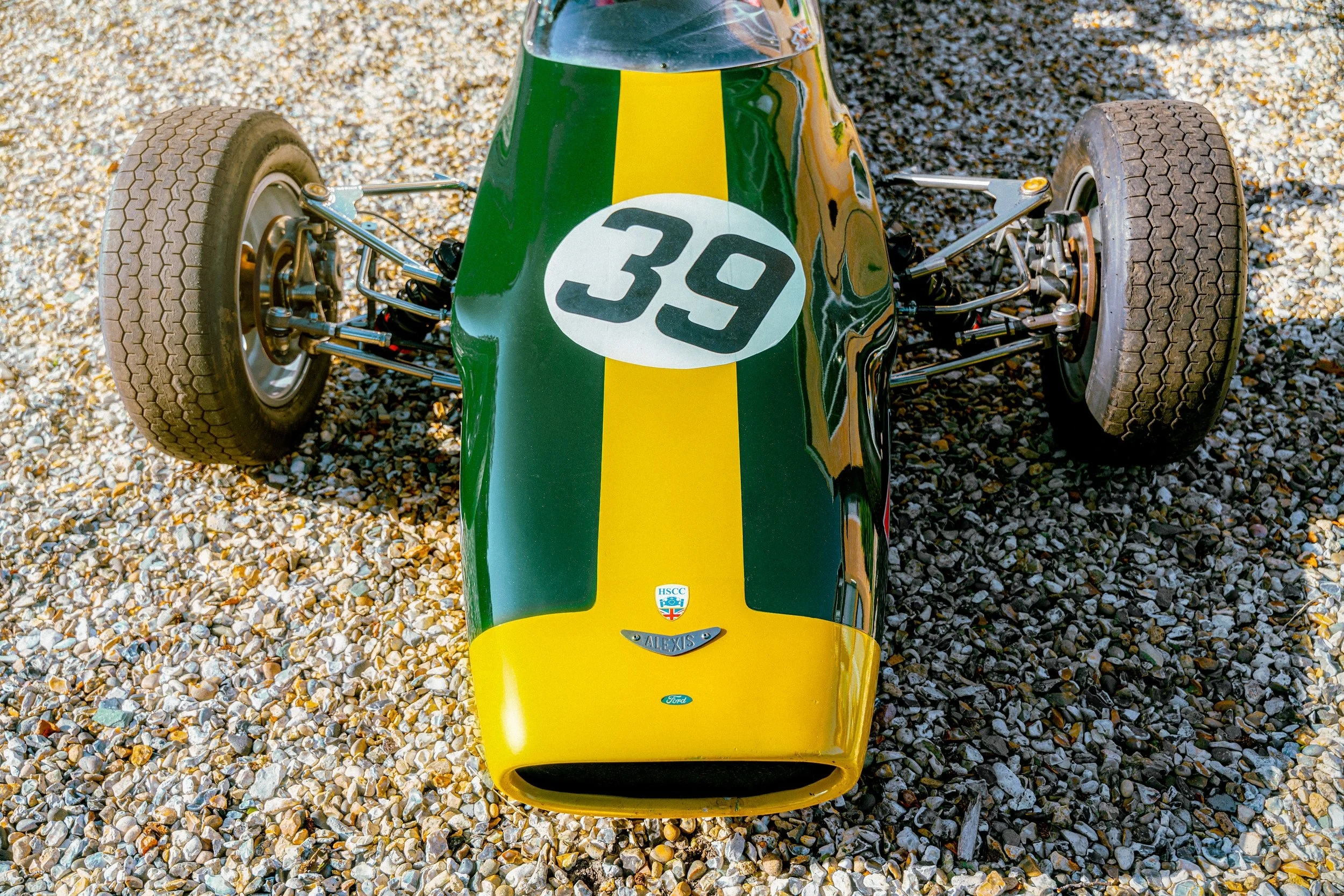 A vintage racing car with a green and yellow paint job, featuring the number 39, on a gravel surface.
