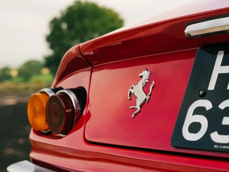 Close-up of the rear end of a red Ferrari sports car, showing the Ferrari emblem and part of the license plate.