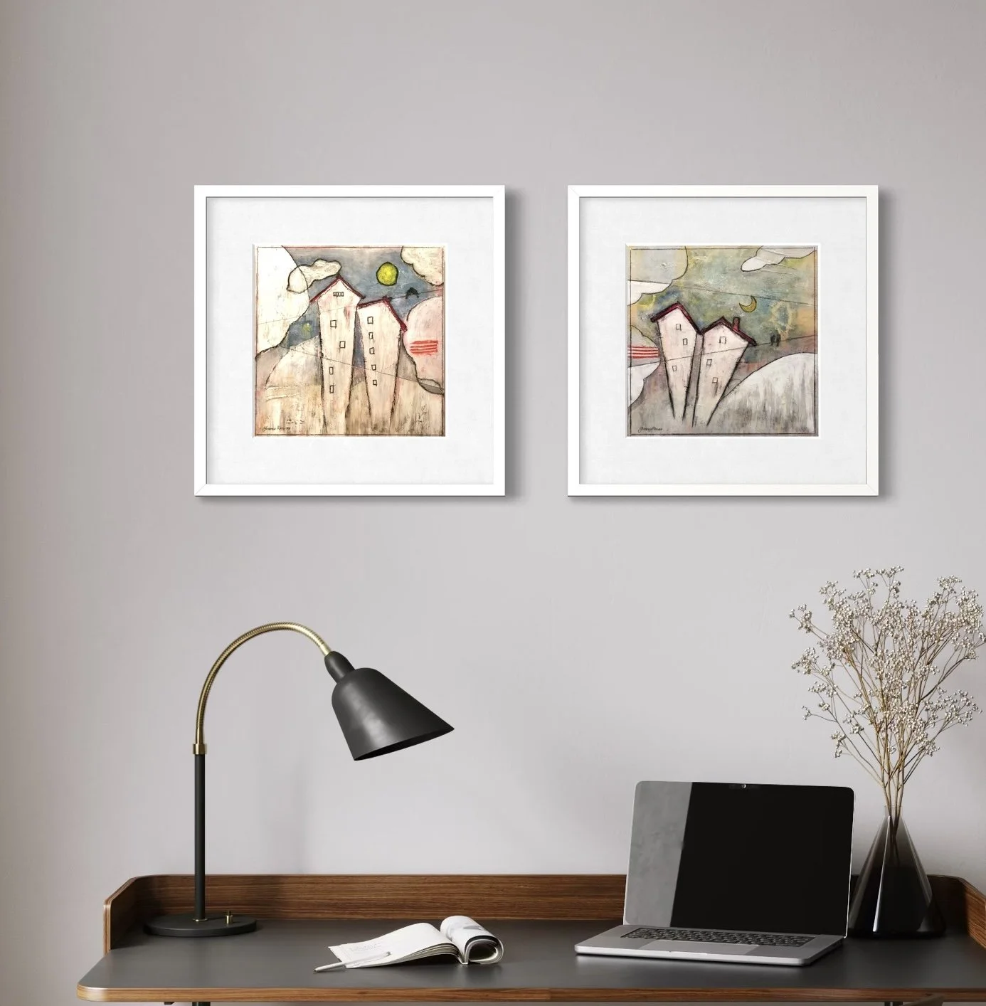 Home office desk with an open notebook, a laptop, a modern desk lamp, and a vase with dried flowers. Two framed abstract open edition prints hang on the light gray wall above the desk.