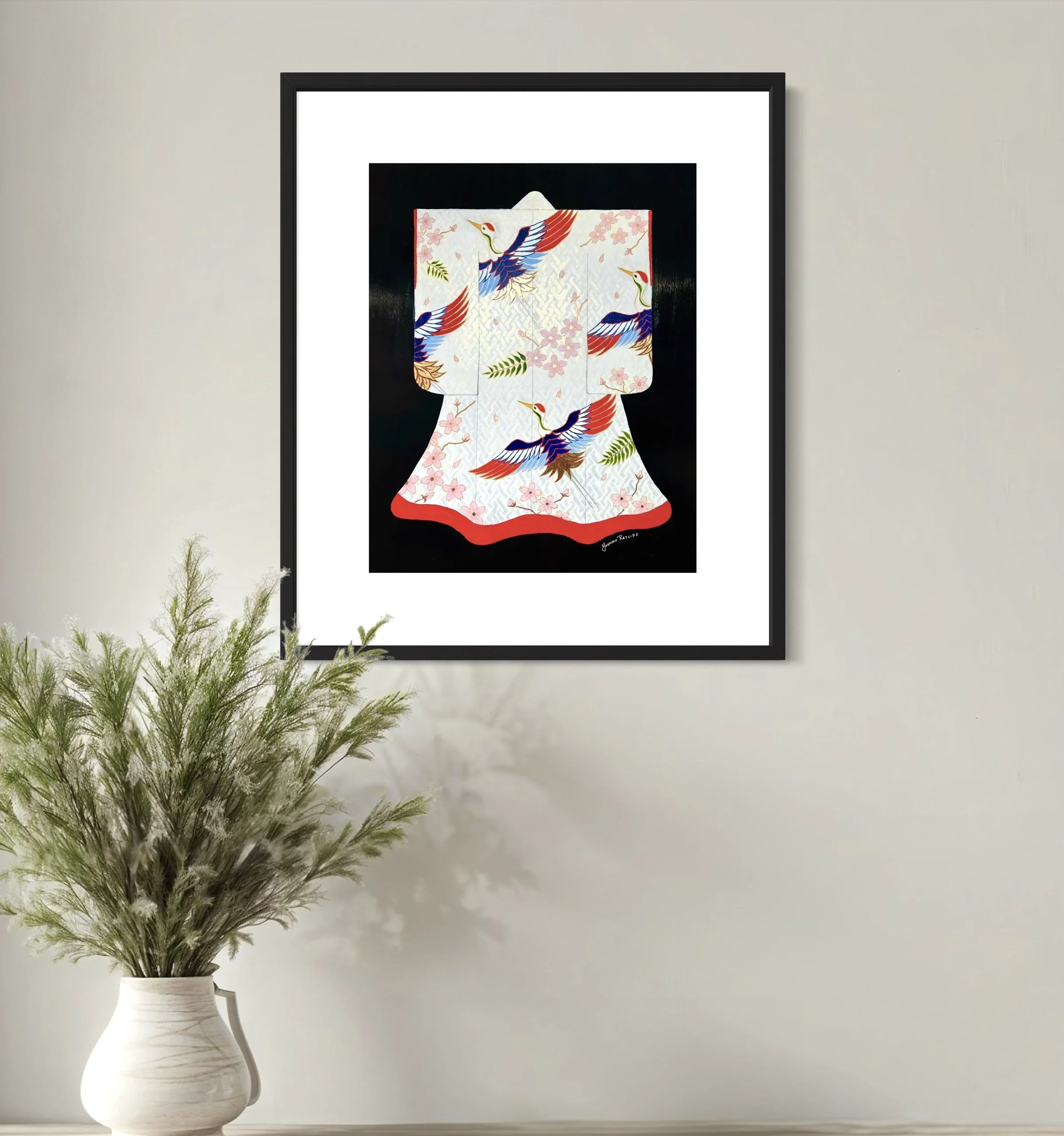 A framed limited edition print, a traditional Japanese kimono with colorful crane and cherry blossom motifs on a black background hanging on light gray wall in the background.