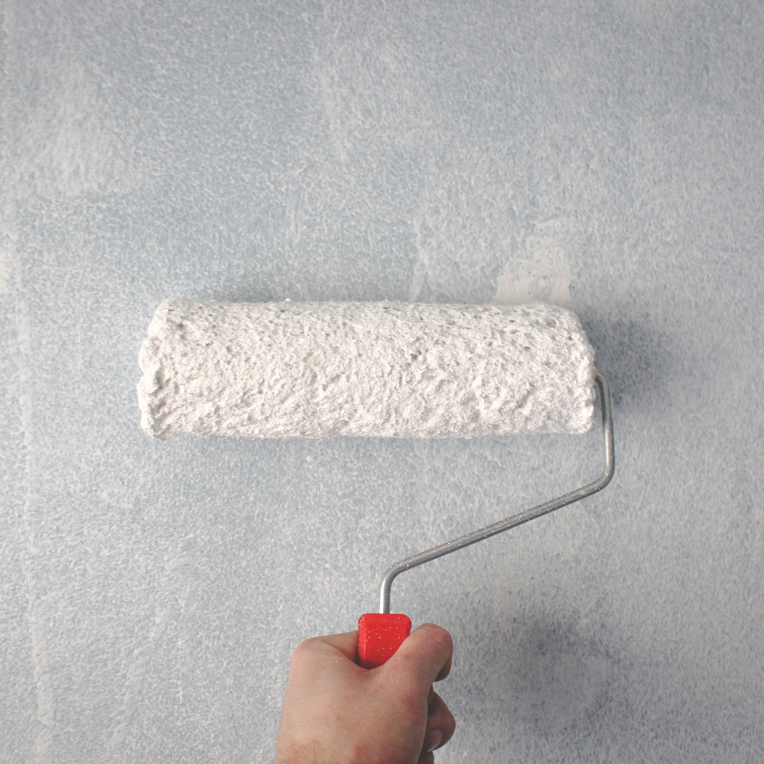 Person using a paint roller with white paint on a wall