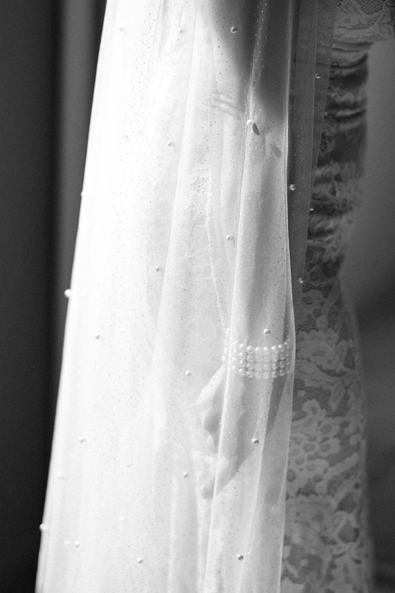it is a photo that shows the body of bride from bellow the chest until the hips. it is black and white. The bride wears a beautiful veil and her hand is under the veil, holding it. The photo focuses to the hand under the veil.