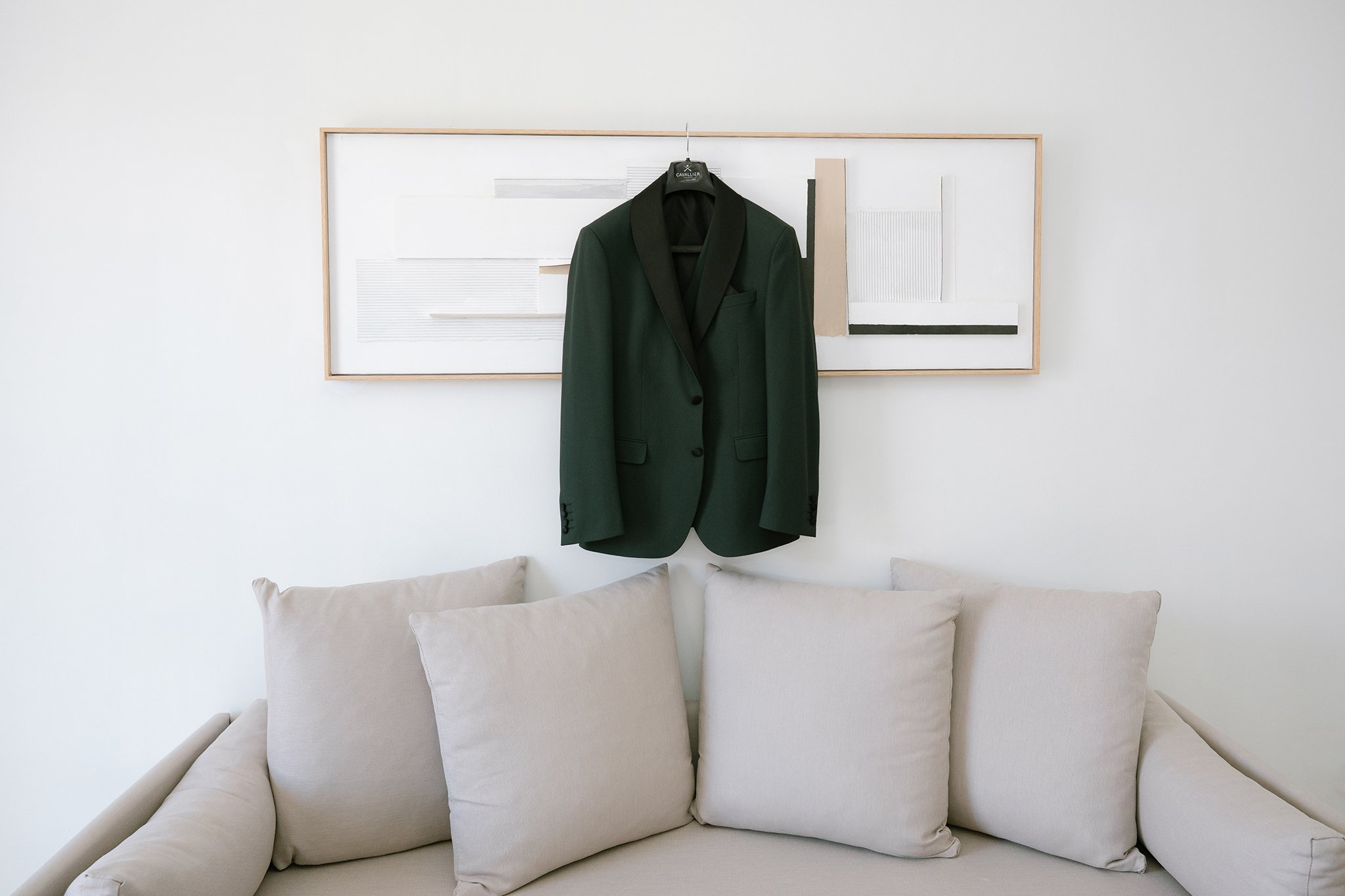 there is a wedding costume in dark green colour hanging for a painting in the living room of s hotel.