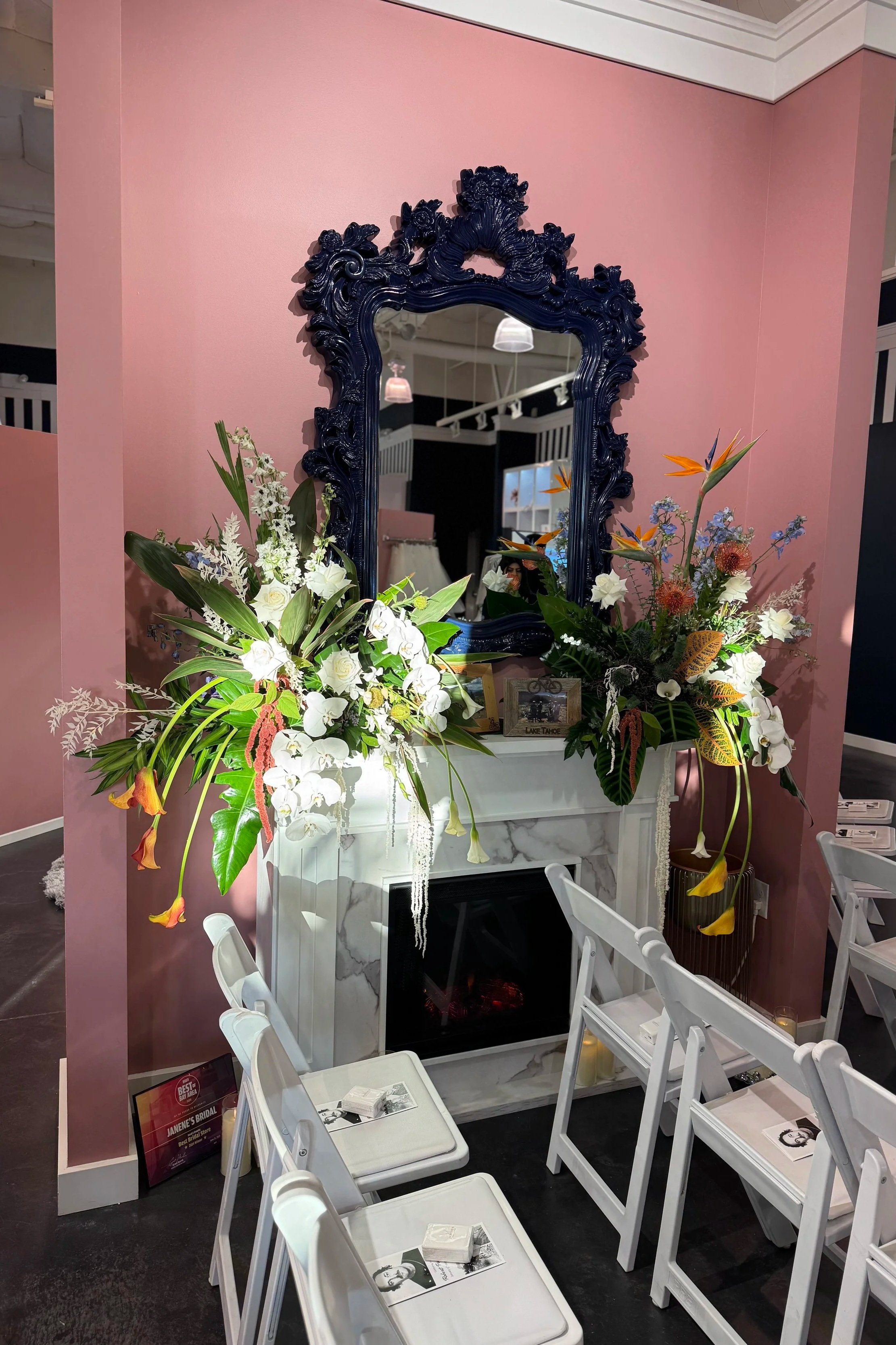 Table setting with white plates and silverware, decorative glasses with green liquid, and a centerpiece of tropical flowers with red blooms and large green leaves.