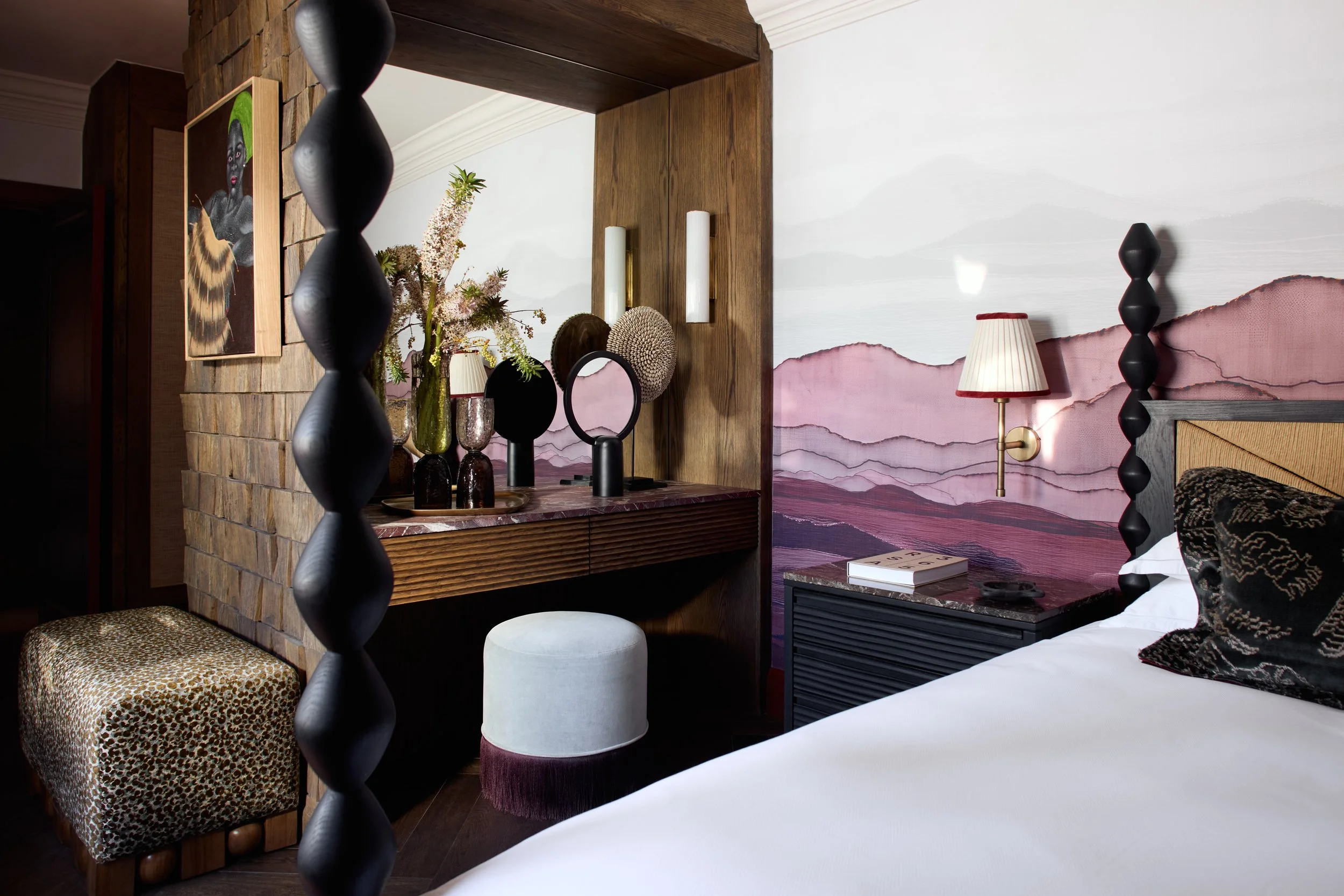 Interior of a bedroom with artistic mountain landscape mural, bedside lamp, decorative items, and furniture.