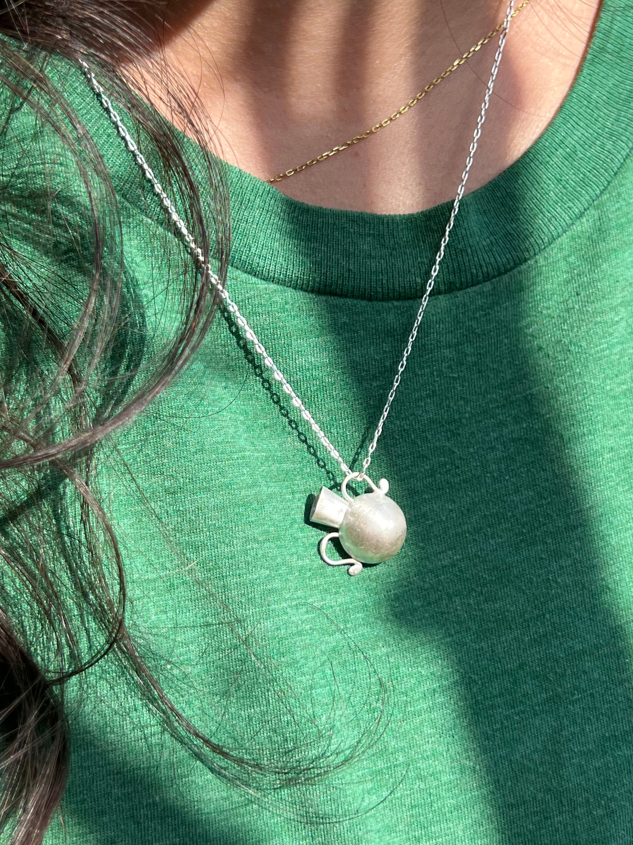 Close-up of a person in a green shirt, wearing a silver necklace.