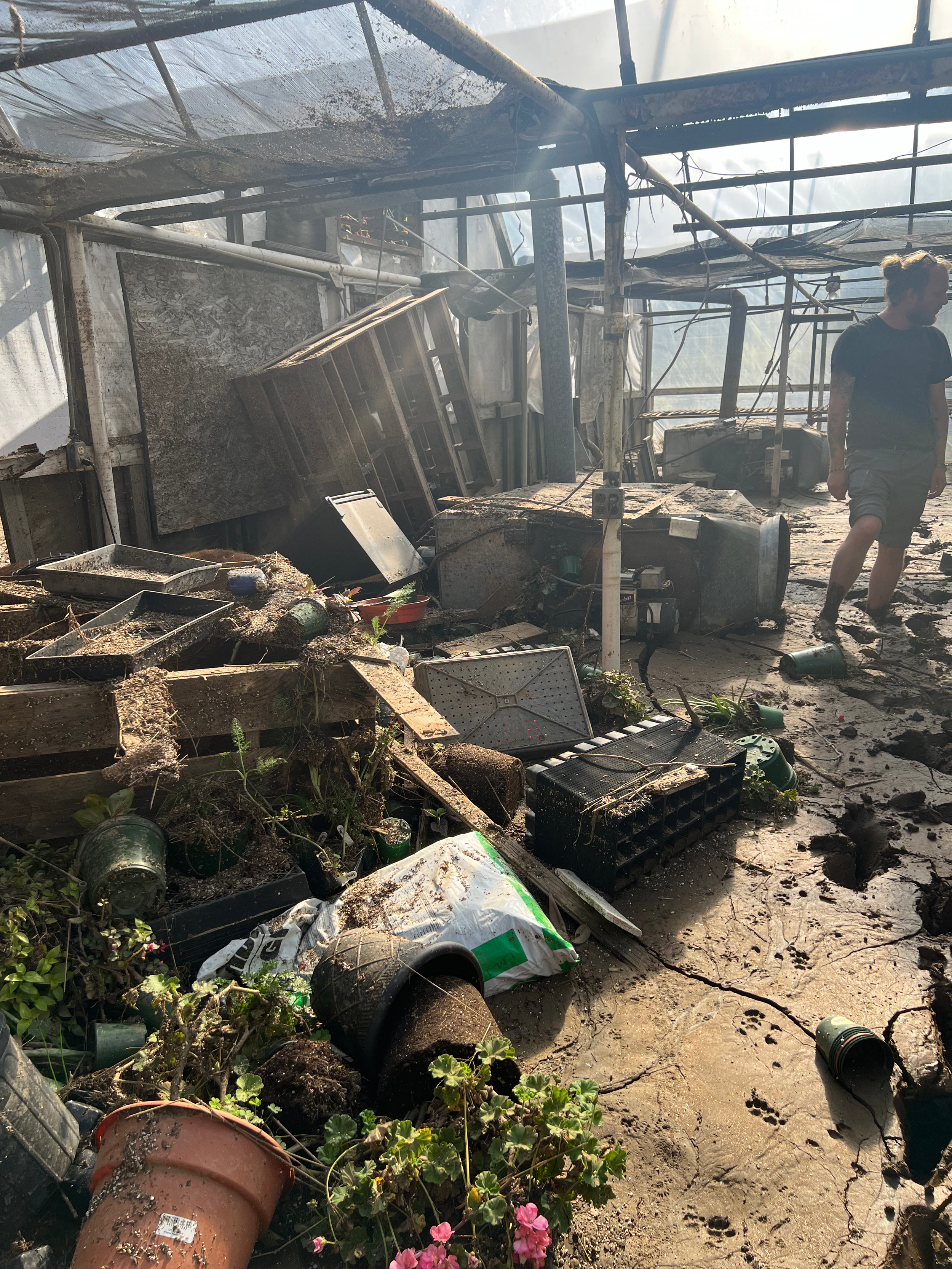 Lakeview's growing greenhouses after hurricane helene, with broken pots, deep mud, and debris on the ground.