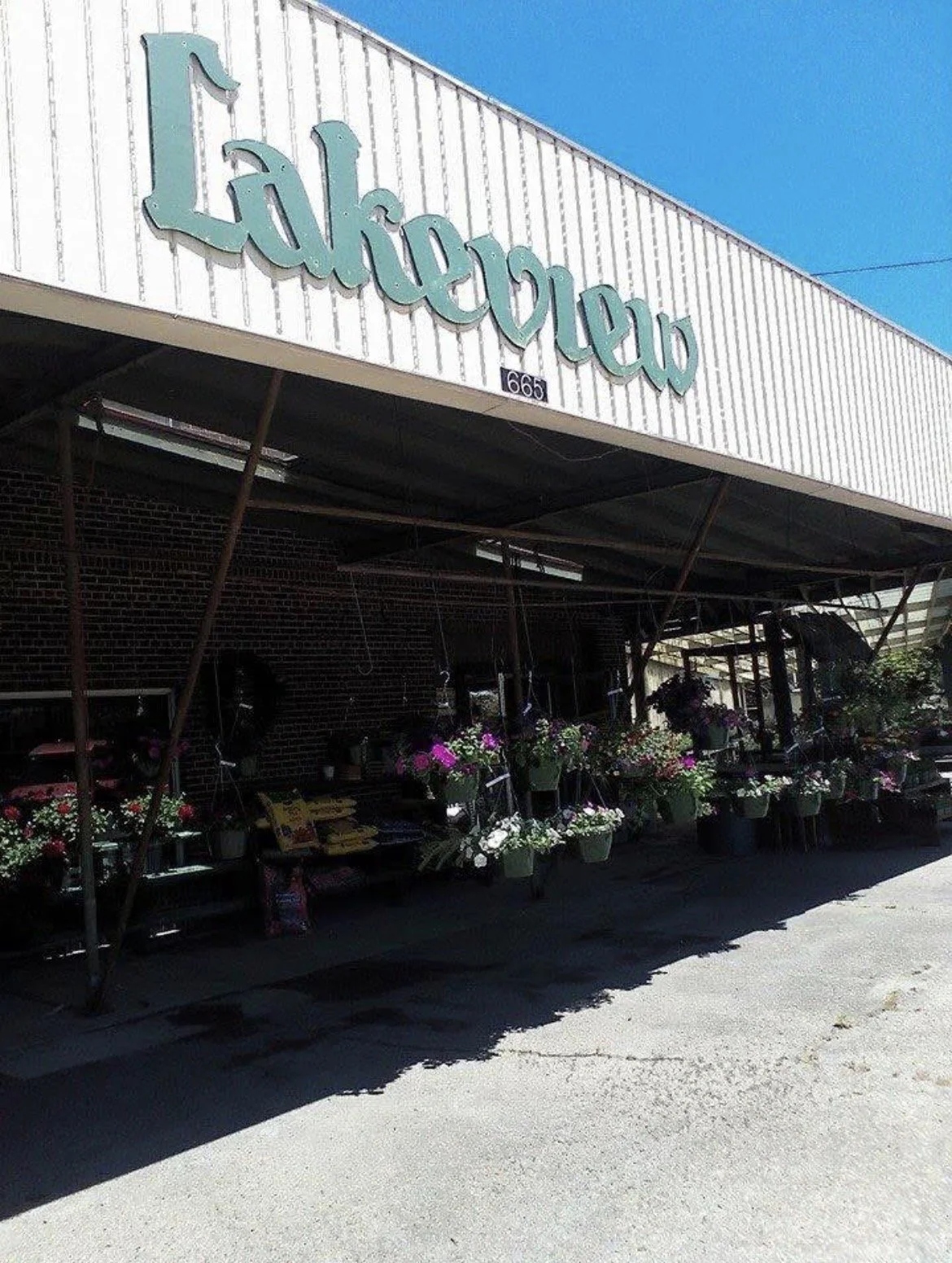 Exterior of the original Lakeview Nursery shop with hanging baskets of colorful flowers and gardening supplies displayed outside.