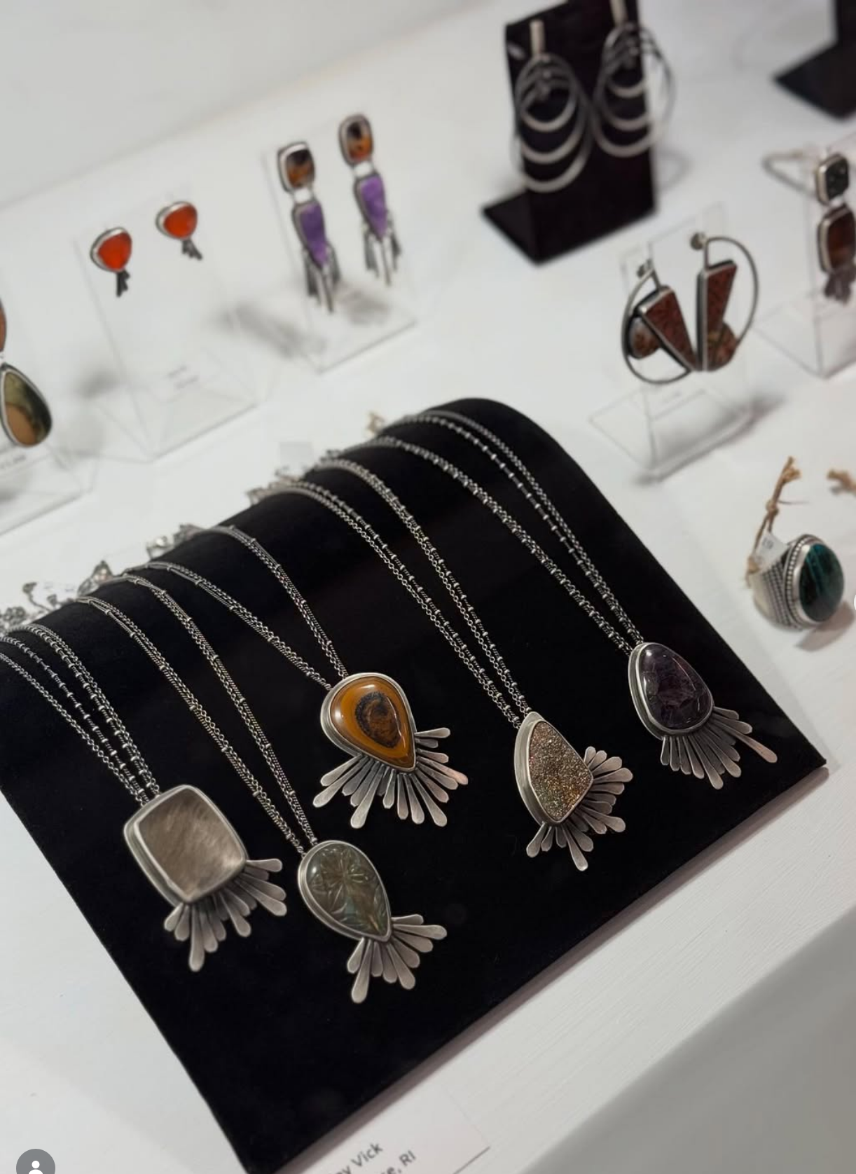 Jewelry display with silver necklaces and colorful gemstones on black velvet, and various earrings on clear stands.