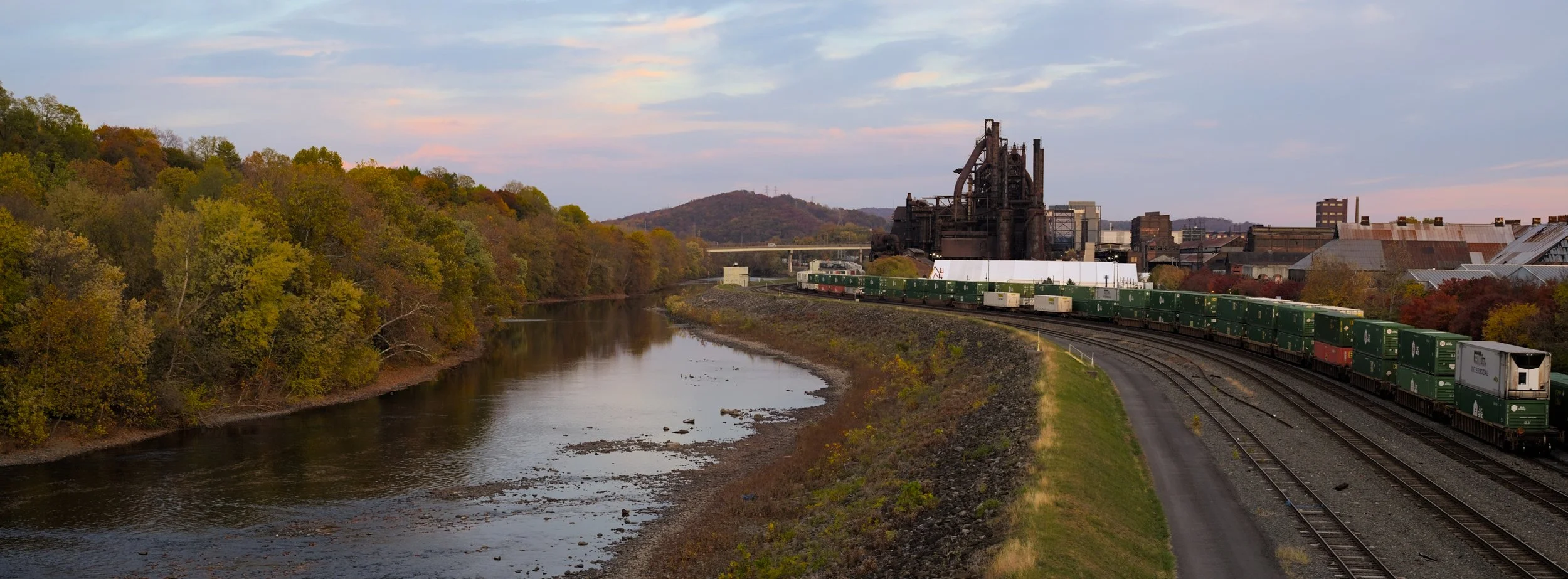 Photograph of the Steel Stacks in Bethlehem, Pennsylvania. Photo taken at sunset, featuring cargo train tracks and the Lehigh river.