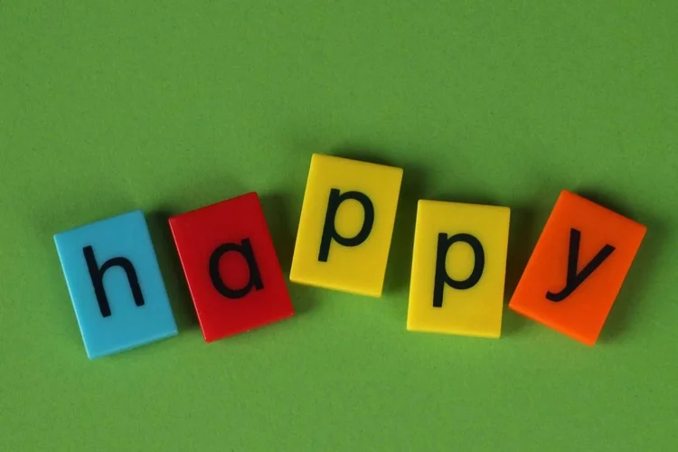 Coloured letter tiles spelling the word happy on a green background.