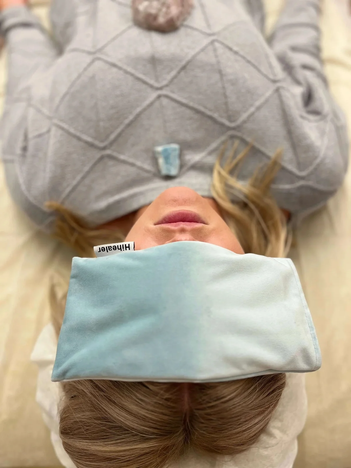 A woman lying on her back wearing a light blue headband and cap, with a gray shirt, in a medical or dental setting.
