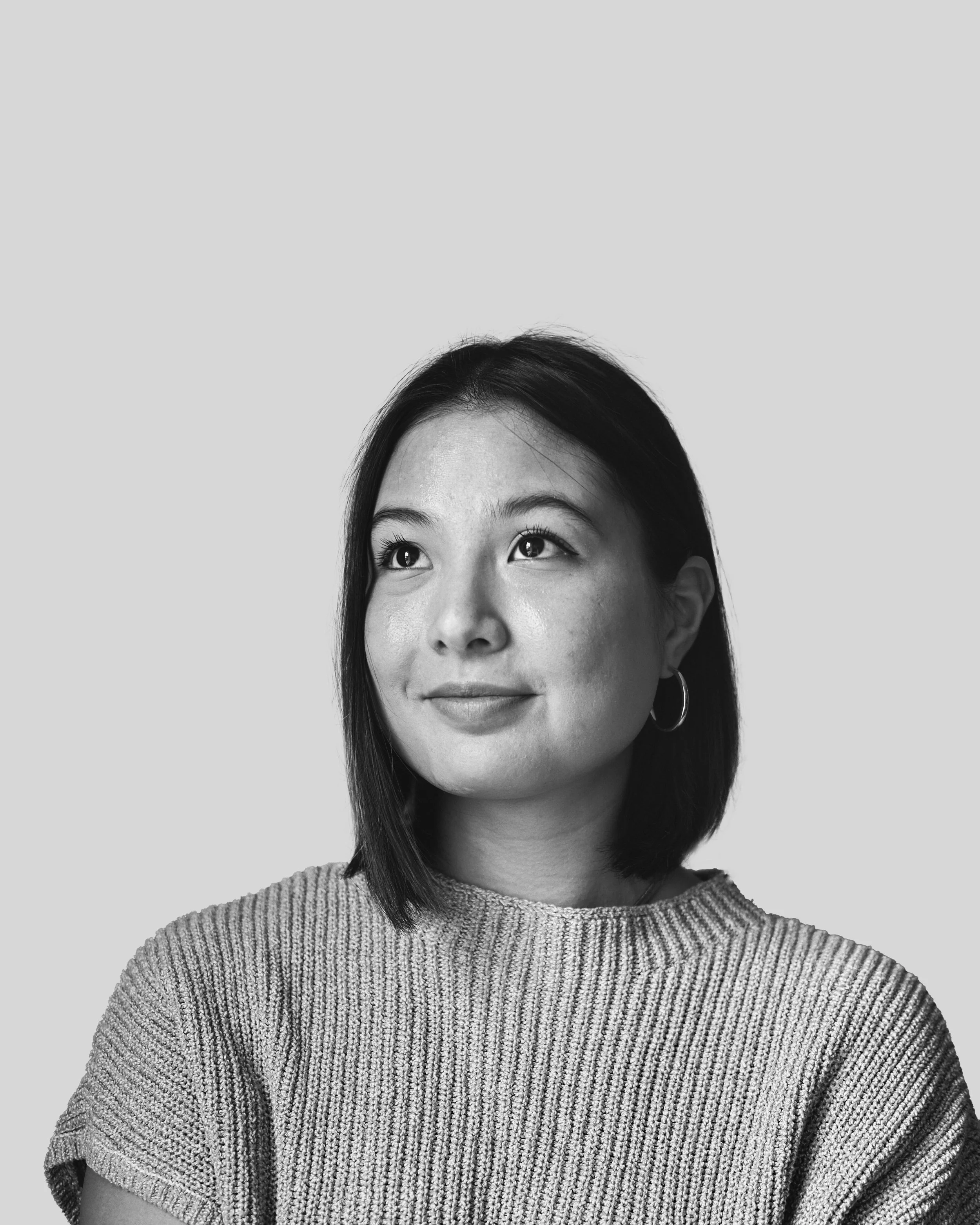Black and white portrait of a woman, named Natalie Wong, looking upward, wearing a knit sweater and hoop earrings.