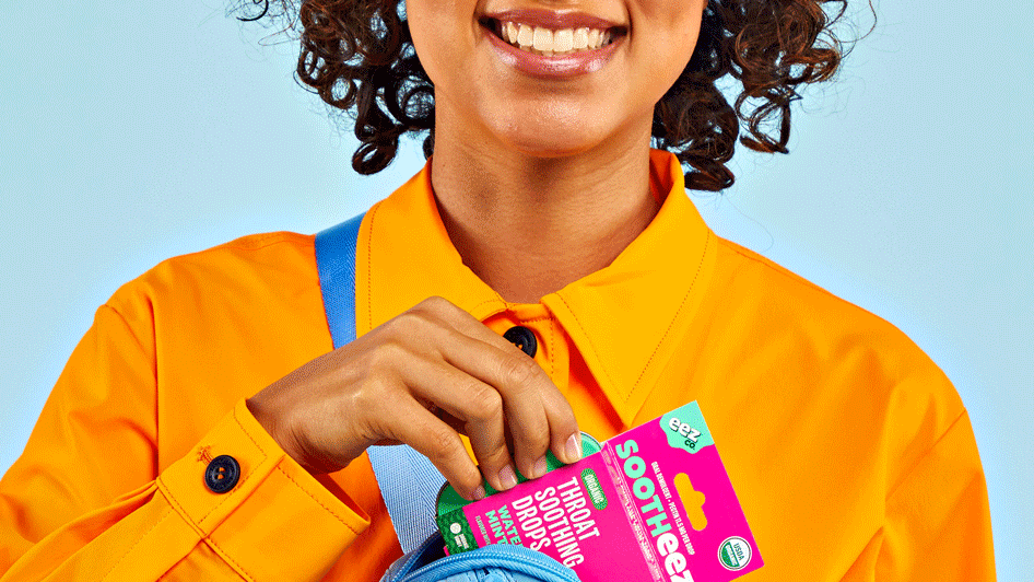 Person in an orange shirt holding a pack of EEZ Company's throat soothing drops near a blue bag.