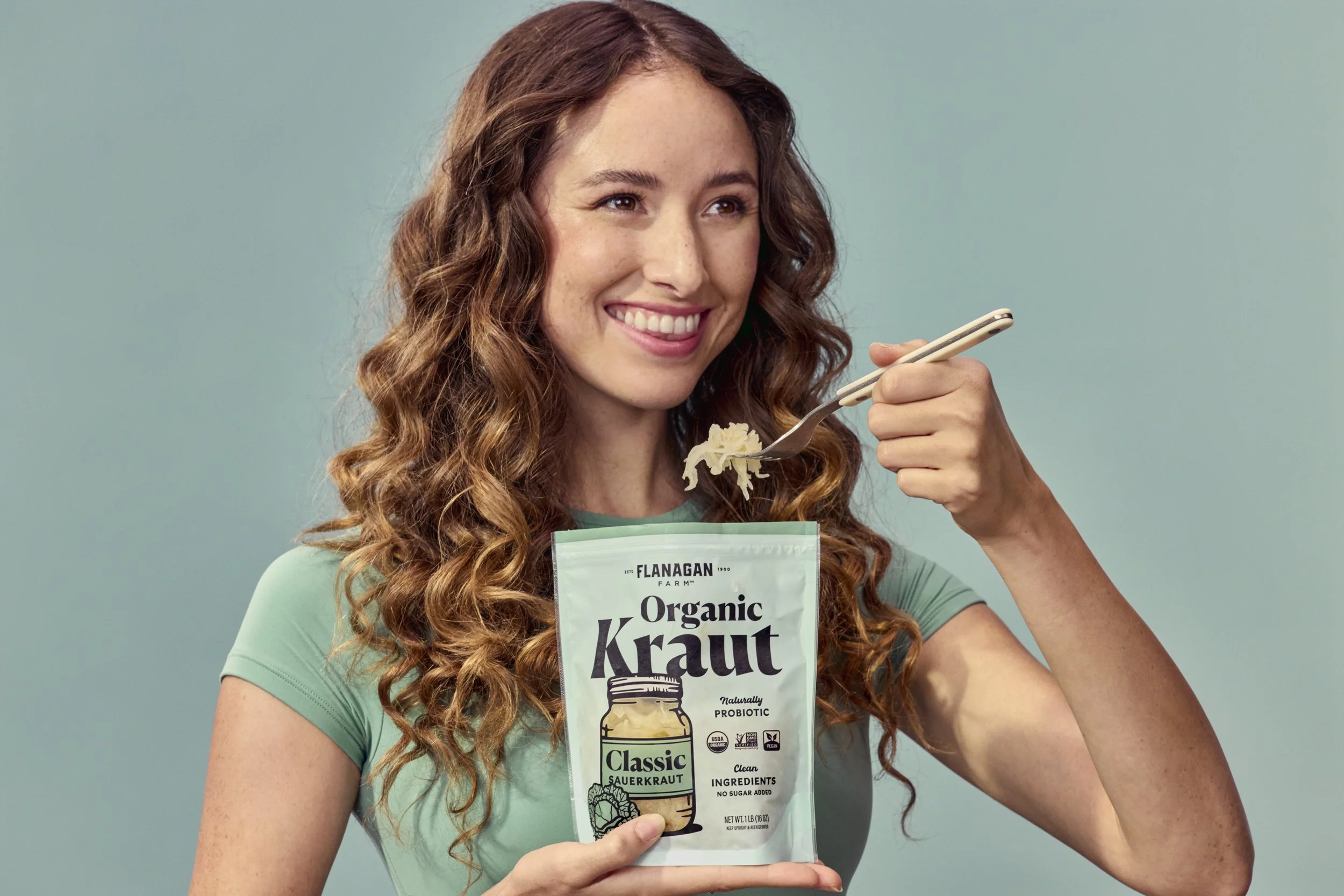 Woman smiling, holding and eating from a pouch of organic sauerkraut.