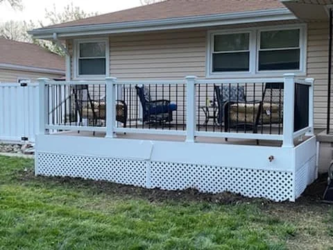 A backyard deck with several chairs and a small table, attached to a house with beige siding.