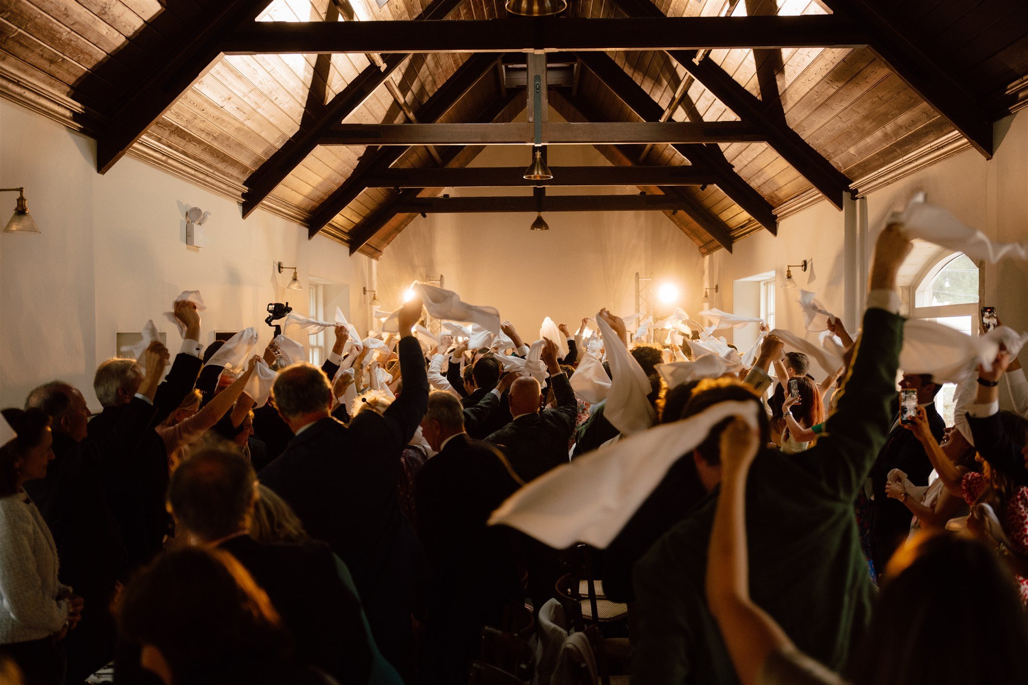 Crowd of people inside a large hall, waving white cloths in the air during a celebration.